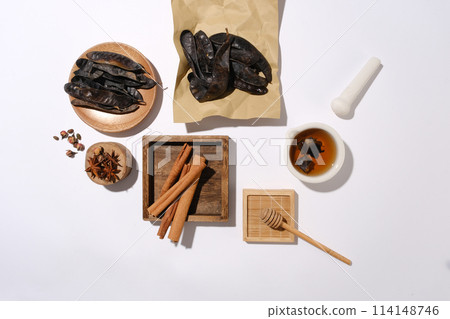 A group of raw materials evenly spread on white table, a rectangle wooden tray contains cinnamon, some locust fruit placed on brown paper and a round dish, a wooden podium with anise on. Template for A group of raw materials evenly spread on white table, a rectangle wooden tray contains cinnamon, some locust fruit placed on brown paper and a round dish, a wooden podium with anise on. Template for 114148746