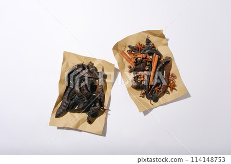 Photography from above, natural ingredients including locust, cinnamon, anise and dried rose buds displayed on two brown paper isolated on white background. Space for text or designing Photography from above, natural ingredients including locust, cinnamon, anise and dried rose buds displayed on two brown paper isolated on white background. Space for text or designing 114148753