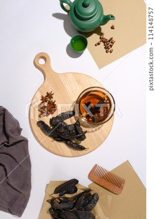 High angle view vertical photo with wooden chopping board contains black locust pods and star anise in center, surrounded by some other ingredients and utensils. Photo for advertise hair care product High angle view vertical photo with wooden chopping board contains black locust pods and star anise in center, surrounded by some other ingredients and utensils. Photo for advertise hair care product 114148757