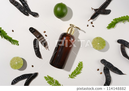 Unlabeled bottle featured on white background, decorated by black locust pods, lemon, and fern branches neatly arrange. Black locust pods helps stimulates hair growth and makes hair stronger Unlabeled bottle featured on white background, decorated by black locust pods, lemon, and fern branches neatly arrange. Black locust pods helps stimulates hair growth and makes hair stronger 114148882