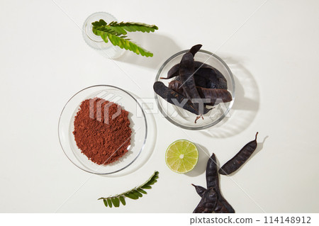 Glass dish of black locust pods placed by a glass bowl of locust powder, a half of lemon, fern. Top view photography with blank space for advertising Glass dish of black locust pods placed by a glass bowl of locust powder, a half of lemon, fern. Top view photography with blank space for advertising 114148912