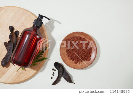A wooden tray with unlabeled bottle above decorated by some black locust pod, next to a wooden dish of black locust powder. Copy space, view from above A wooden tray with unlabeled bottle above decorated by some black locust pod, next to a wooden dish of black locust powder. Copy space, view from above 114148925