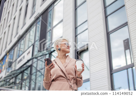 businesswoman using mobile phone and holding coffee cup against urban background businesswoman using mobile phone and holding coffee cup against urban background 114149052