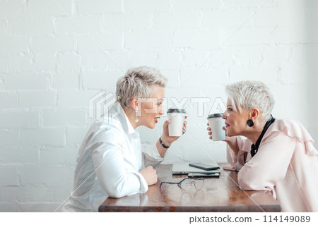 Two female senior collegues sitting next to each other in an cafe Two female senior collegues sitting next to each other in an cafe 114149089