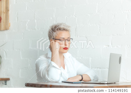 Smiling businesswoman is sitting at table with laptop and using think about business Smiling businesswoman is sitting at table with laptop and using think about business 114149191