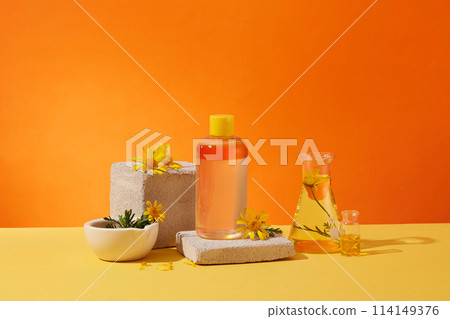 Front view of cosmetic bottle with ingredient from calendula extract displayed on brick podium. Fresh calendula flower, lab flask full of liquid on orange background Front view of cosmetic bottle with ingredient from calendula extract displayed on brick podium. Fresh calendula flower, lab flask full of liquid on orange background 114149376