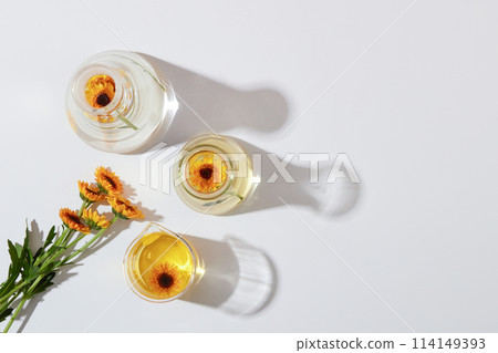 Mockup scene for cosmetic of calendula extract. Top view of fresh calendula flowers on lab glassware with essence decorated on a white background. Minimal concept, copy space 114149393