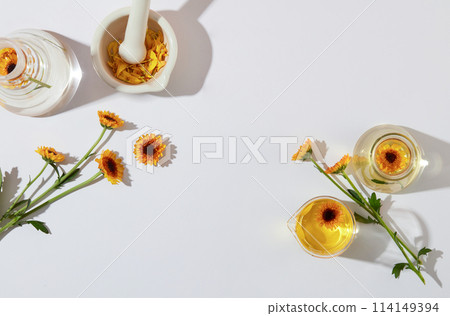 Fresh calendula flowers decorated with glass flask and small mortar and pestle on a white background. Concept for advertising cosmetics product extracted from calendula with space for presentation 114149394