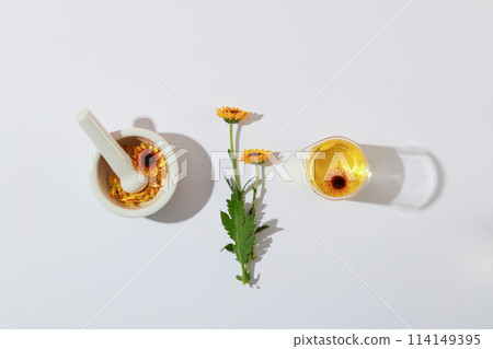 Small mortar and pestle, fresh calendula and beaker containing calendula extract decorated on a white background. Advertising photo with minimal concept and blank space for display product Small mortar and pestle, fresh calendula and beaker containing calendula extract decorated on a white background. Advertising photo with minimal concept and blank space for display product 114149395