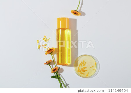 Top view of fresh calendula with petri dish and yellow bottle unlabeled for toner on a white background. Advertising cosmetics of calendula extract. Herbs are widely used in cosmetics. Top view of fresh calendula with petri dish and yellow bottle unlabeled for toner on a white background. Advertising cosmetics of calendula extract. Herbs are widely used in cosmetics. 114149404