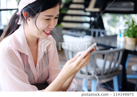 Beautiful Asian businesswoman is smiling and relaxing with smartphone in cafe and coffee shop Beautiful Asian businesswoman is smiling and relaxing with smartphone in cafe and coffee shop 114149973
