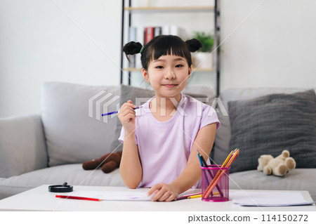 A young girl is sitting at a table with a pencil and a cup of crayons A young girl is sitting at a table with a pencil and a cup of crayons 114150272