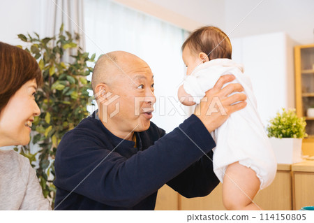 A grandfather holding his baby grandchild at home and a grandmother watching over him 114150805