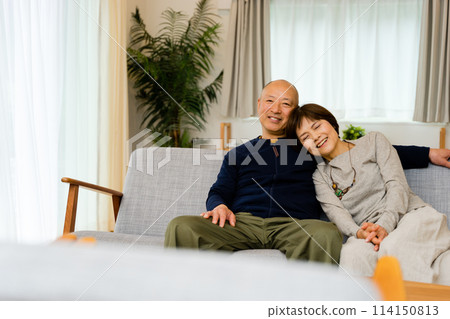 A friendly middle-aged couple in their 50s and 60s sitting close together on a sofa in the living room A friendly middle-aged couple in their 50s and 60s sitting close together on a sofa in the living room 114150813