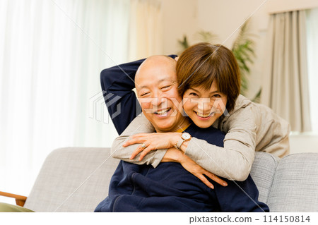A very close senior couple in their 50s and 60s hugging on the sofa in their living room at home A very close senior couple in their 50s and 60s hugging on the sofa in their living room at home 114150814