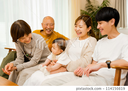 A newborn baby sits on his mother's lap while his father and grandparents watch over him. 114150819
