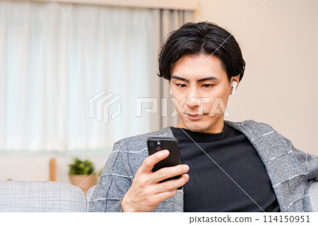 一名 30 多歲的男子在客廳操作智慧型手機 一名 30 多歲的男子在客廳操作智慧型手機 114150951