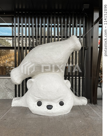 Adorable and cute polar bear statue in a playful mood with a milk bottle balancing on its back, isolated on a white background. 114152896