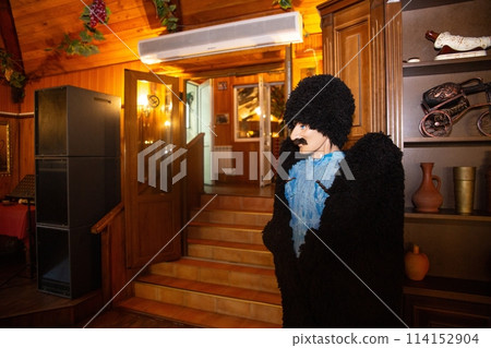 A man with a beard and mustache is wearing a fur coat and hat. He is standing in a restaurant with a rustic interior. 114152904