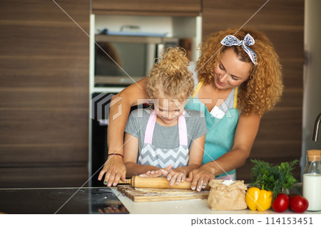 Beautiful young mom and her cute little daughter rolling out dough at home. 114153451