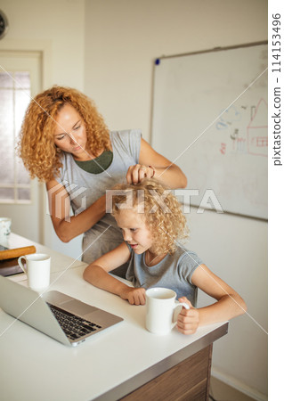 Smiling Mother helps her adorable daughter with homework at living room Smiling Mother helps her adorable daughter with homework at living room 114153496