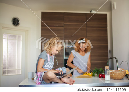 Little girl and her daughter baking cookies at home, reading recipe on laptop. Little girl and her daughter baking cookies at home, reading recipe on laptop. 114153509