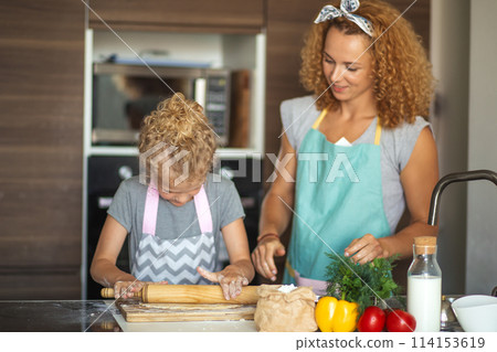 Beautiful young mom and her cute little daughter rolling out dough at home. 114153619