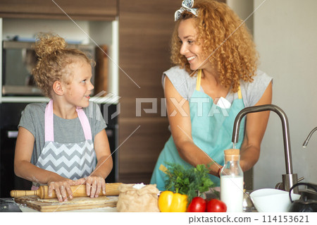 Beautiful young mom and her cute little daughter rolling out dough at home. 114153621