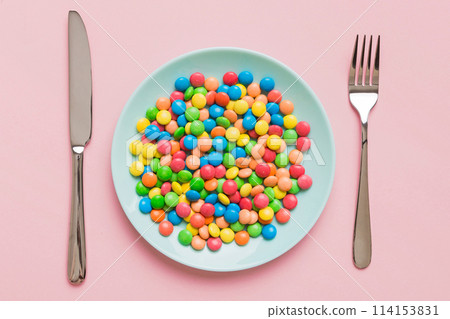 cutlery on table and sweet plate of candy. Health and obesity concept, top view on colored background cutlery on table and sweet plate of candy. Health and obesity concept, top view on colored background 114153831