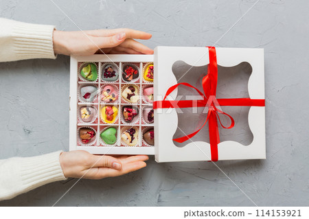 Female hands with delicious candies in box on color background Female hands with delicious candies in box on color background 114153921