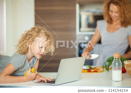 Little girl and her daughter baking cookies at home, reading recipe on laptop. Little girl and her daughter baking cookies at home, reading recipe on laptop. 114154254