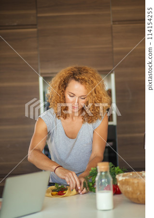 Little girl and her daughter baking cookies at home, reading recipe on laptop. Little girl and her daughter baking cookies at home, reading recipe on laptop. 114154255