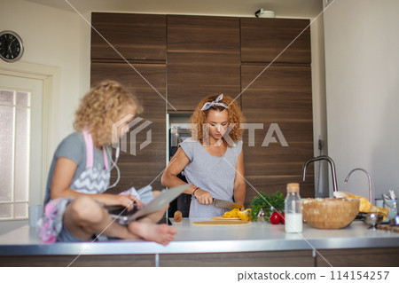 Little girl and her daughter baking cookies at home, reading recipe on laptop. 114154257