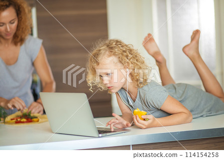 Little girl and her daughter baking cookies at home, reading recipe on laptop. Little girl and her daughter baking cookies at home, reading recipe on laptop. 114154258