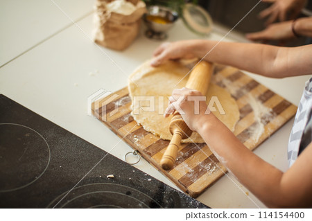 Beautiful young mom and her cute little daughter rolling out dough at home. 114154400
