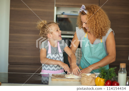 Woman and cute daughter cooking on kitchen, making dough for birthday party. 114154434
