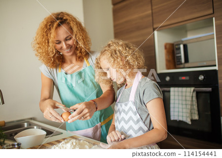 Woman and cute daughter cooking on kitchen, making dough for birthday party. 114154441