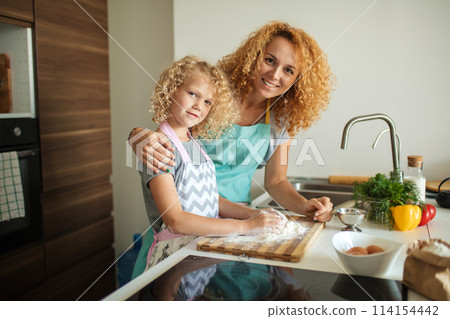 Woman and cute daughter cooking on kitchen, making dough for birthday party. 114154442