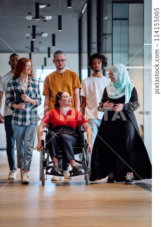A diverse group of young business people walking a corridor in the glass-enclosed office of a modern startup, including a person in a wheelchair and a woman wearing a hijab 114155005