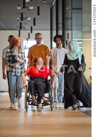 A diverse group of young business people walking a corridor in the glass-enclosed office of a modern startup, including a person in a wheelchair and a woman wearing a hijab A diverse group of young business people walking a corridor in the glass-enclosed office of a modern startup, including a person in a wheelchair and a woman wearing a hijab 114155023
