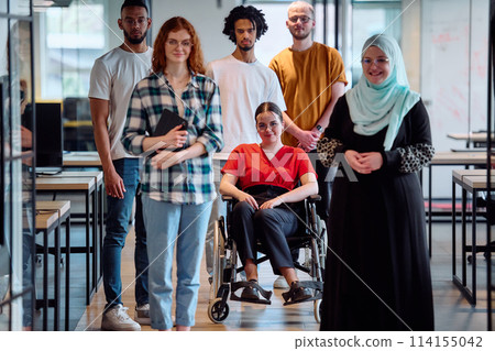A diverse group of young business people walking a corridor in the glass-enclosed office of a modern startup, including a person in a wheelchair and a woman wearing a hijab 114155042