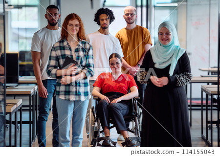 A diverse group of young business people walking a corridor in the glass-enclosed office of a modern startup, including a person in a wheelchair and a woman wearing a hijab 114155043