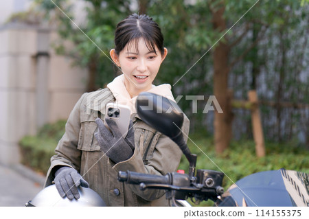 A woman riding a motorcycle with a smartphone A woman riding a motorcycle with a smartphone 114155375