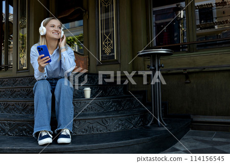 A girl in headphones and with a phone on the street. A girl in headphones and with a phone on the street. 114156545