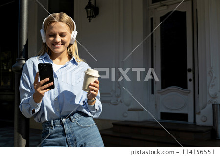A girl in headphones and with a phone on the street. 114156551