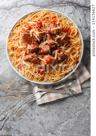 Slow stewed beef in wine tomato sauce served with spaghetti close-up in a plate. Vertical top view Slow stewed beef in wine tomato sauce served with spaghetti close-up in a plate. Vertical top view 114156627