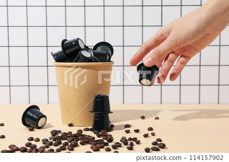 Black coffee capsules in paper cup, hand and coffee beans on light background 114157902