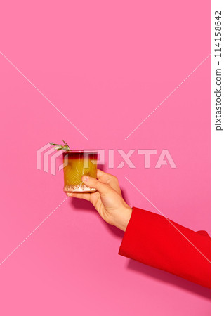 Female hand holding cocktail with orange juice against pink background. New York sour traditional cocktail 114158642