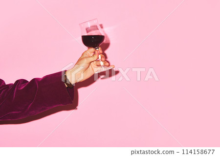 Male hand holding glass with red wine against pink background. Celebration, degustation Male hand holding glass with red wine against pink background. Celebration, degustation 114158677