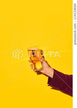 Male hand holding glass with lager beer against bright yellow background. Party time and refreshment 114158684